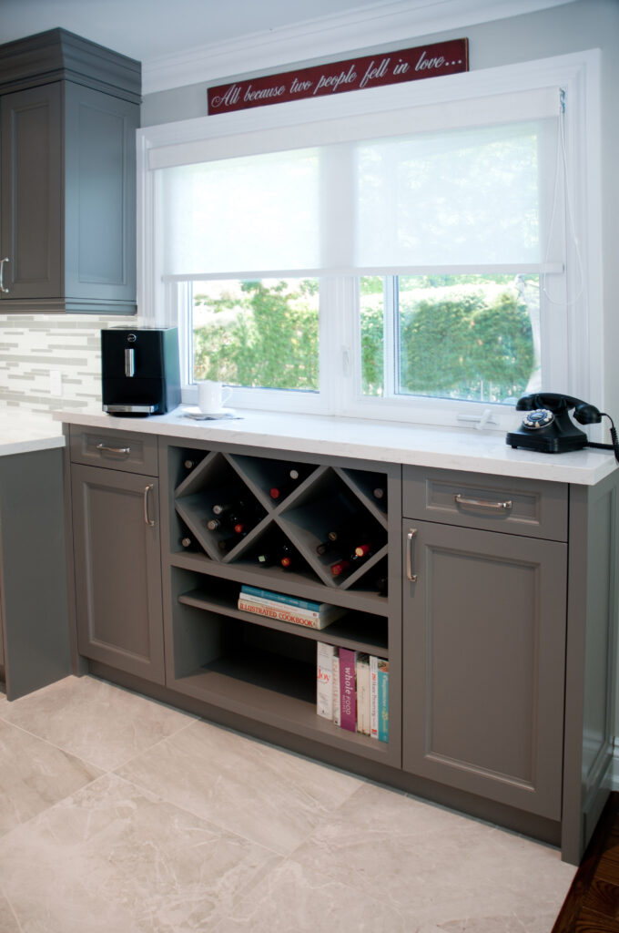 grey kitchen, L shaped kitchen, white countertop, quartz, grey kitchen cabinets, glass cabinets, kitchen desk, kitchen reno, laurndry room reno, stacked washer dryer, tiled floor, chrome, micro hood, microwave hood, slide-in range, wine rack, pendant lights, mudroom, stained glass, charging station